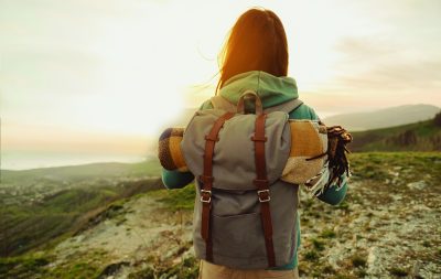 Eine Frau die mit einem Rucksack auf dem Rücken in der Sonne steht und wandert.