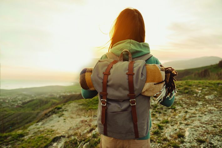 Eine Frau die mit einem Rucksack auf dem Rücken in der Sonne steht und wandert.